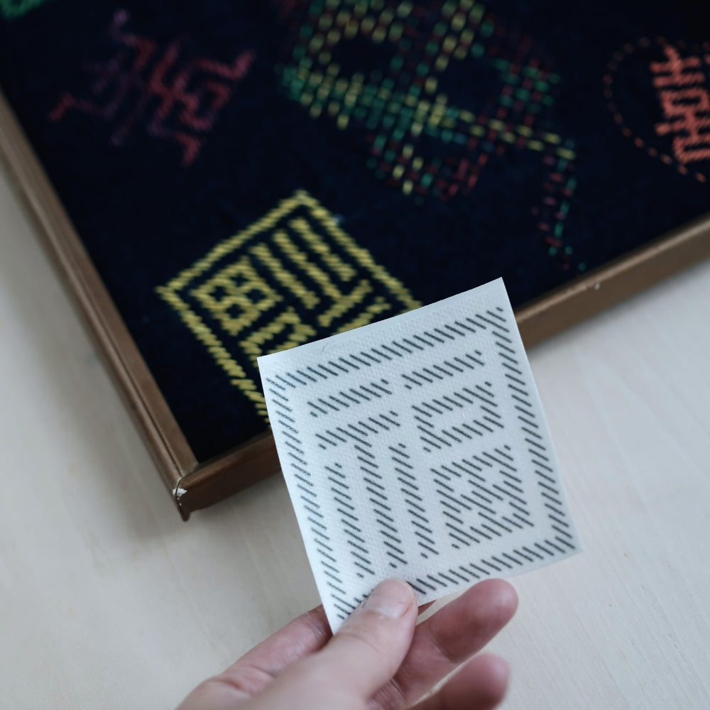 Hand holding a small Fuku character Sashiko sticker with finished embroidery in the background.
