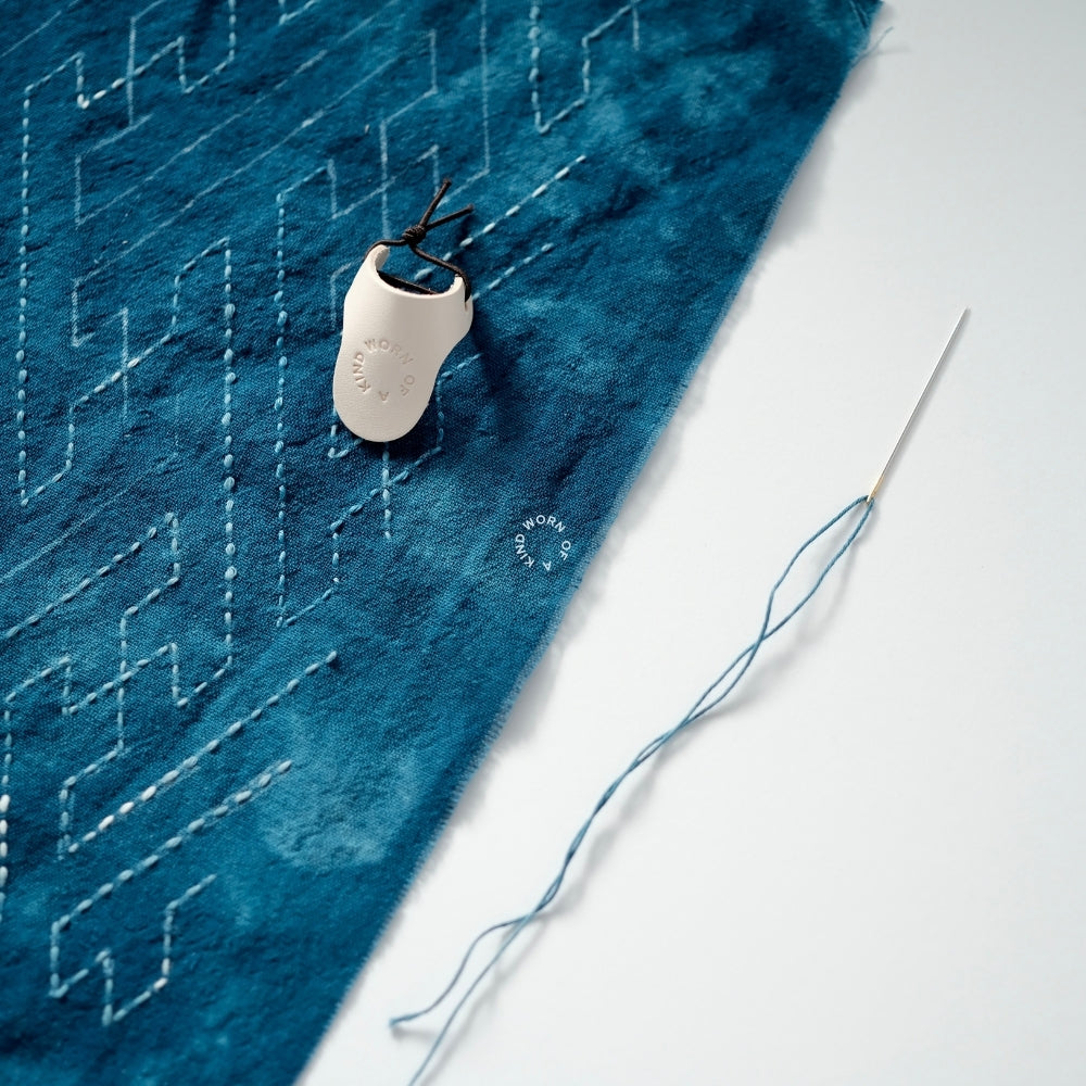 Leather palm thimble resting on a work-in-progress Sashiko mending project.