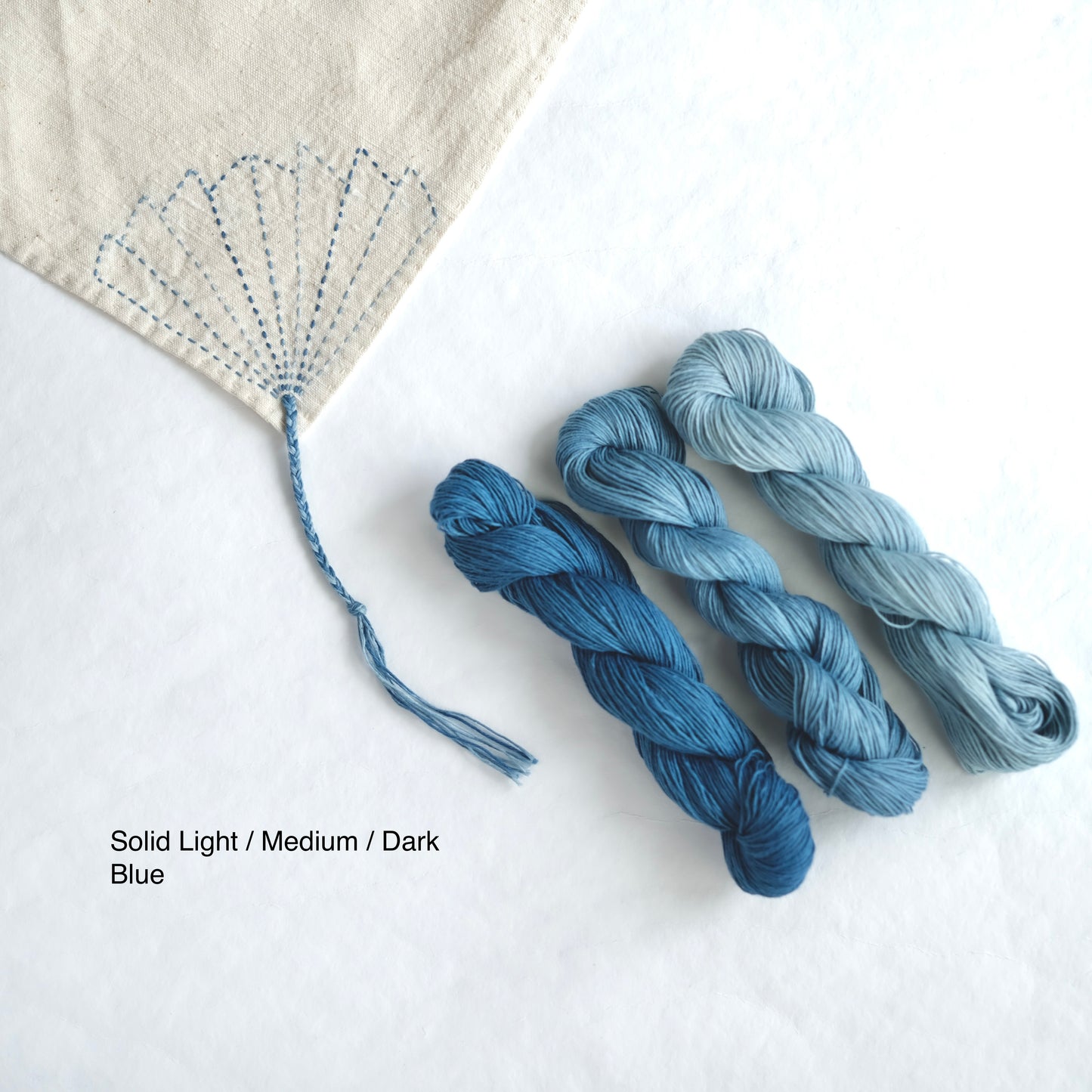 Comparison of solid light, medium, and dark indigo Sashiko thread with fan-shaped stitching.