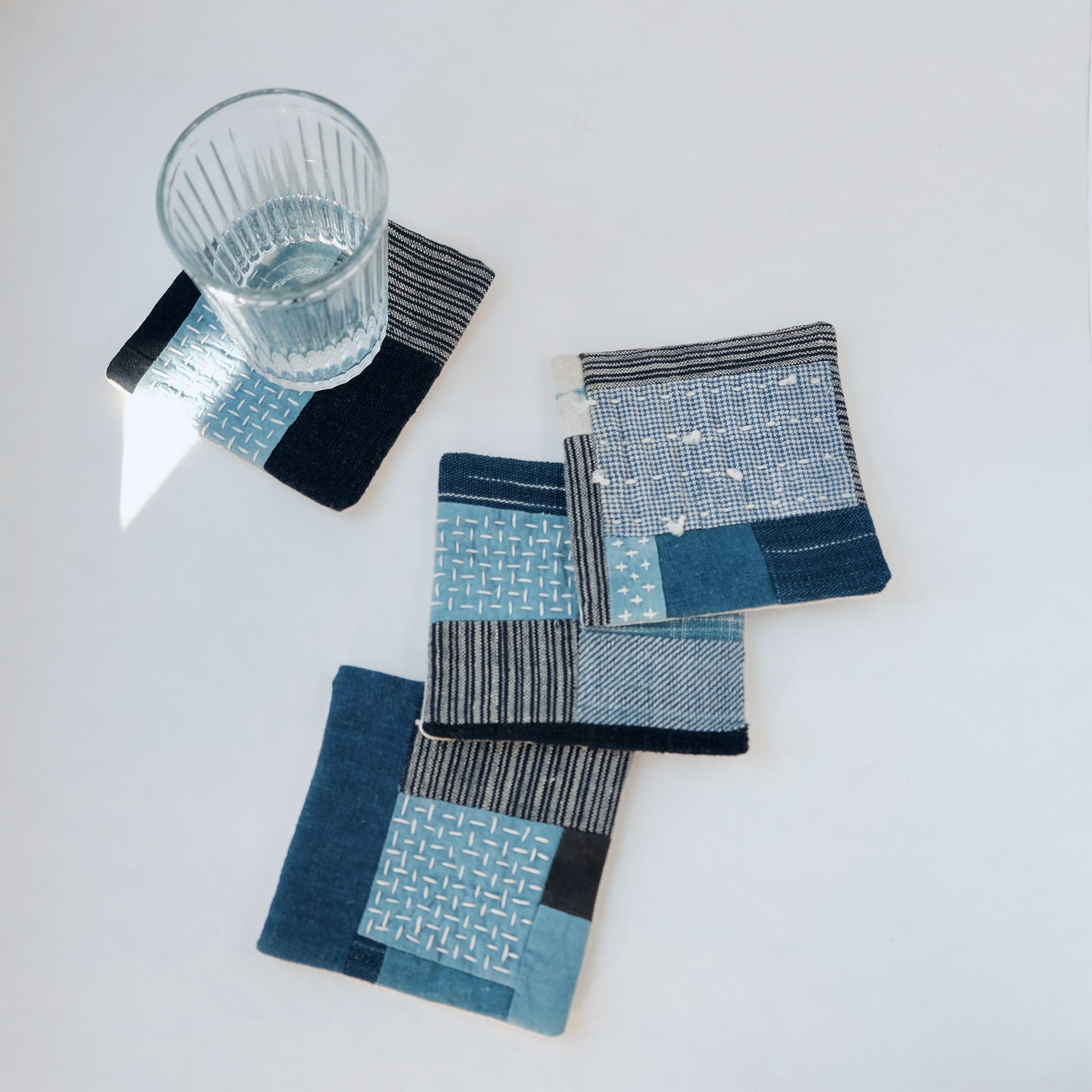 Set of four handcrafted Boro patchwork coasters with glass on indigo fabric.