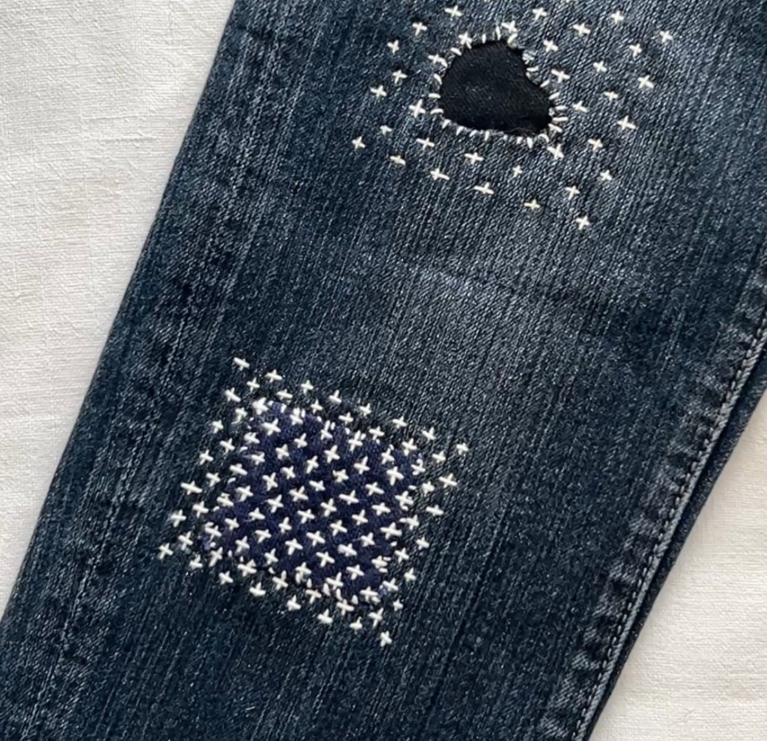 Visible mending on denim jeans using white Hitomezashi sashiko stitching with a Worn of a Kind kit.