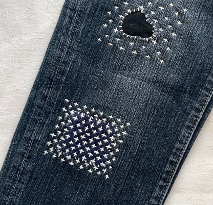 Visible mending on denim jeans using white Hitomezashi sashiko stitching with a Worn of a Kind kit.