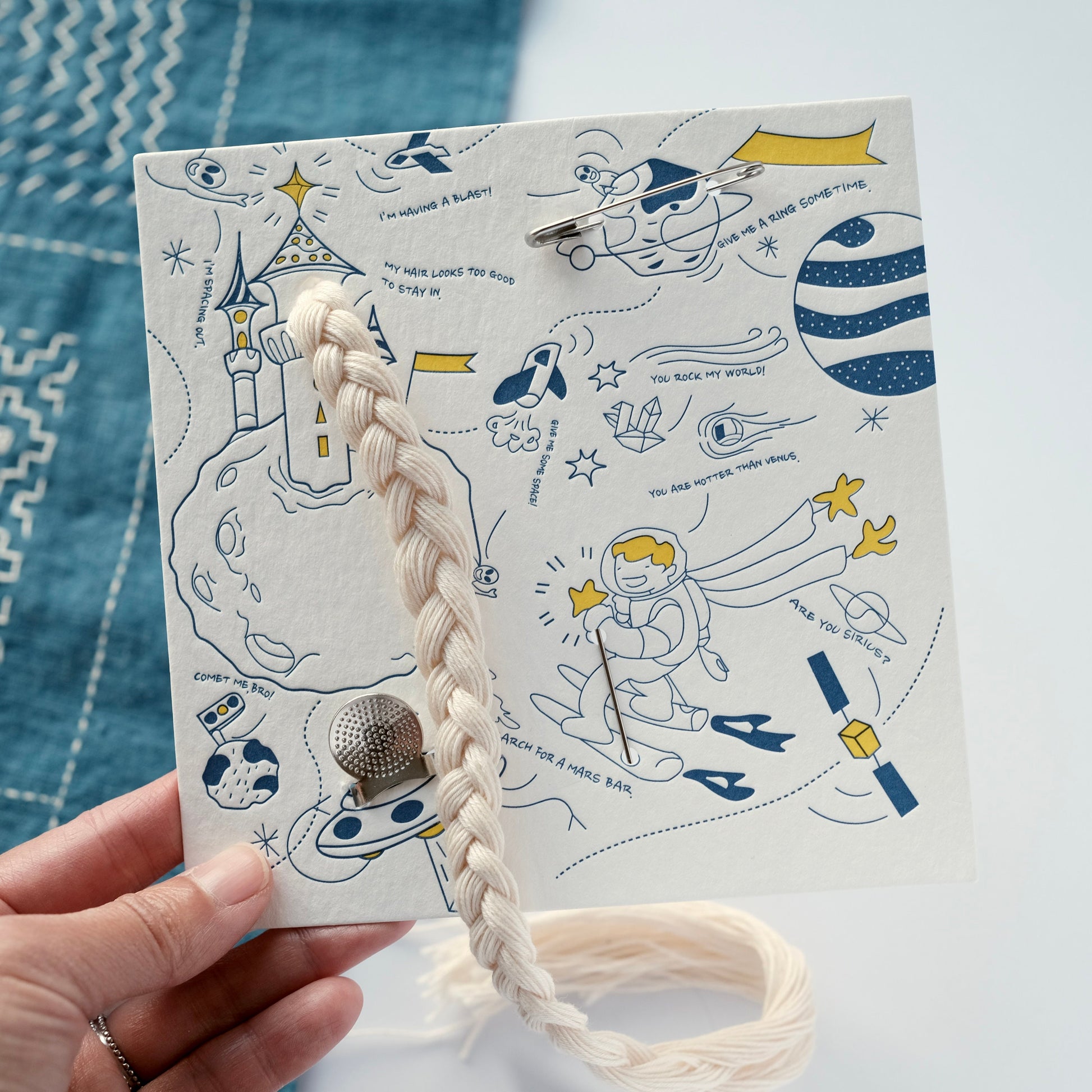 Close-up of the essential Sashiko tools on a card held on hand: Clover thimble, hand-braided thread, and sashiko needles.