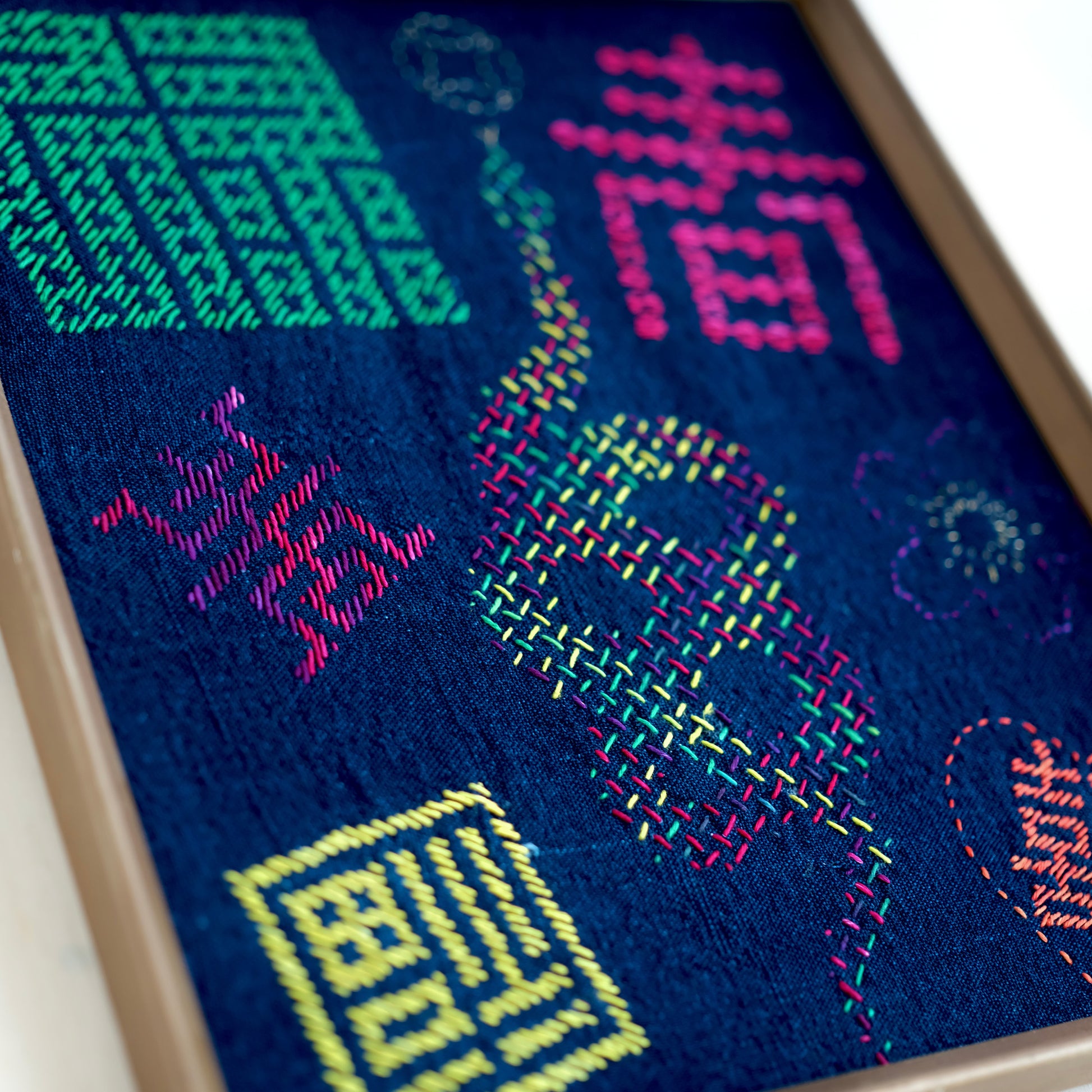 Eight completed sashiko patterns stitched in colorful  thread on a framed indigo blue fabric.