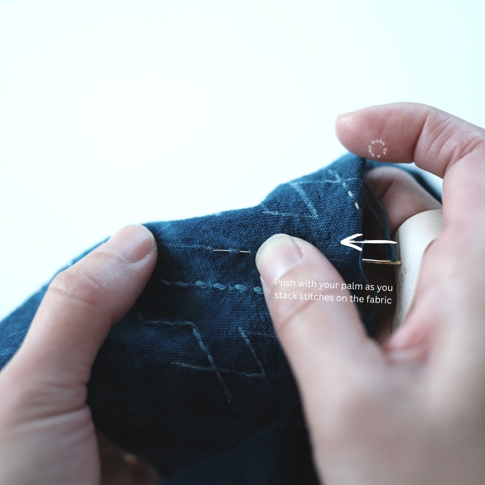 Close-up of hands stacking stitches on indigo fabric using a Sashiko needle.