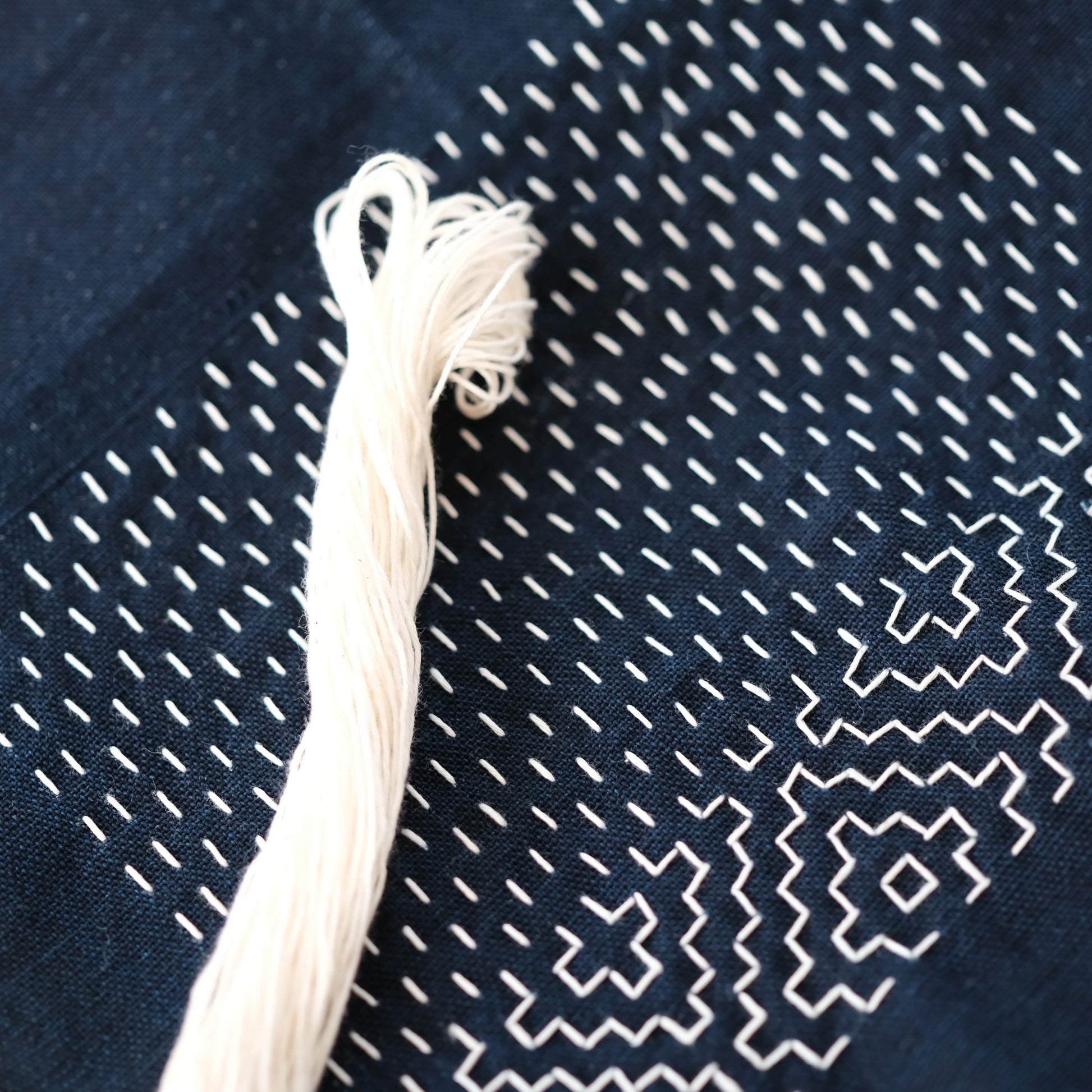 Work-in-progress Hitomezashi pattern on indigo fabric with a 20m skein of natural undyed cotton thread.