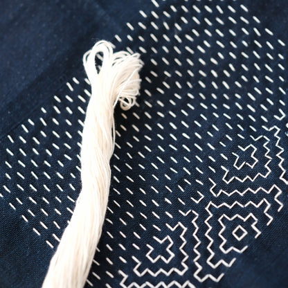 Work-in-progress Hitomezashi pattern on indigo fabric with a 20m skein of natural undyed cotton thread.