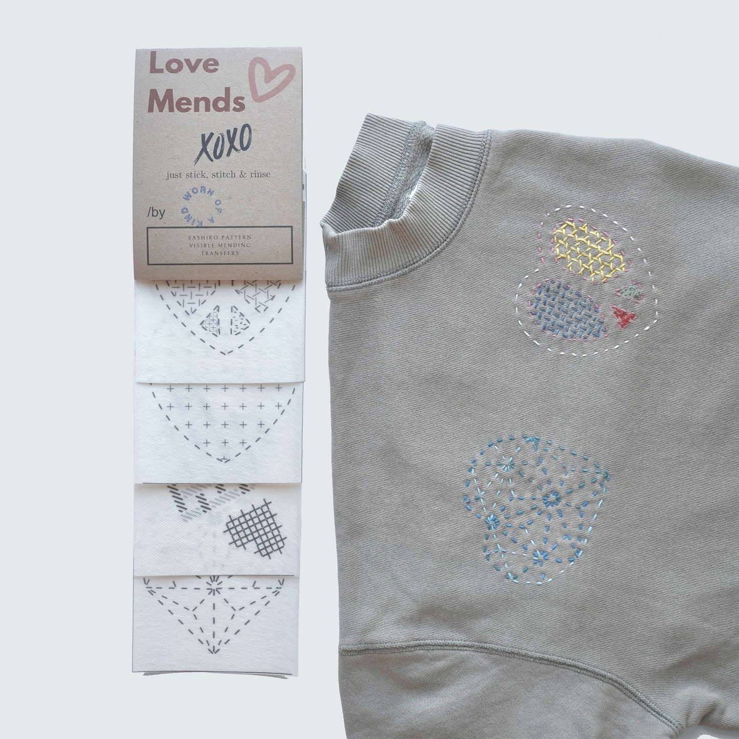 Love Mends Sashiko transfer set with heart-themed patterns sampled on a grey sweatshirt.