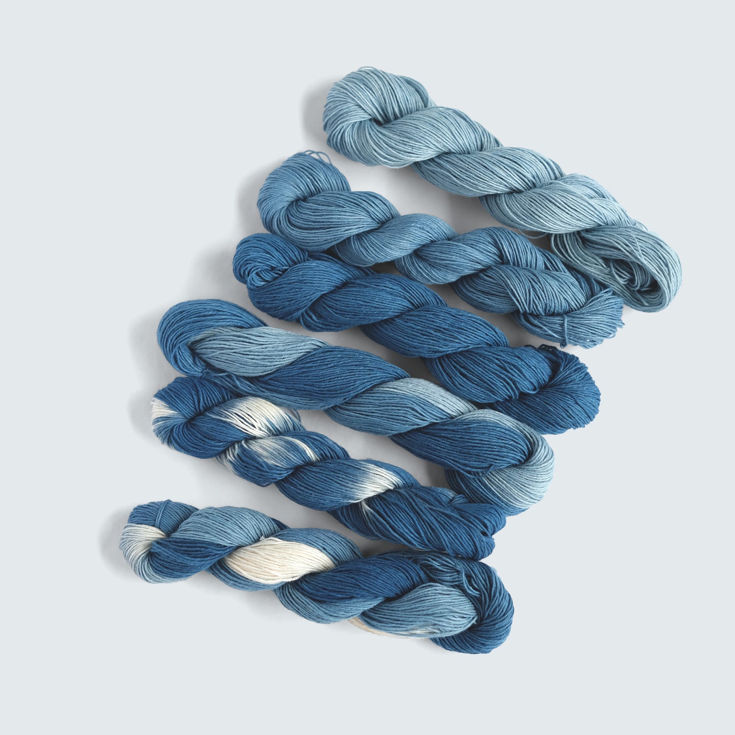 Six shades of hand-dyed organic indigo Sashiko thread including variegated and solid blues.