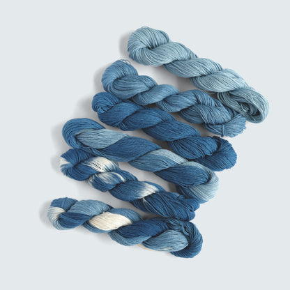 Six shades of hand-dyed organic indigo Sashiko thread including variegated and solid blues.