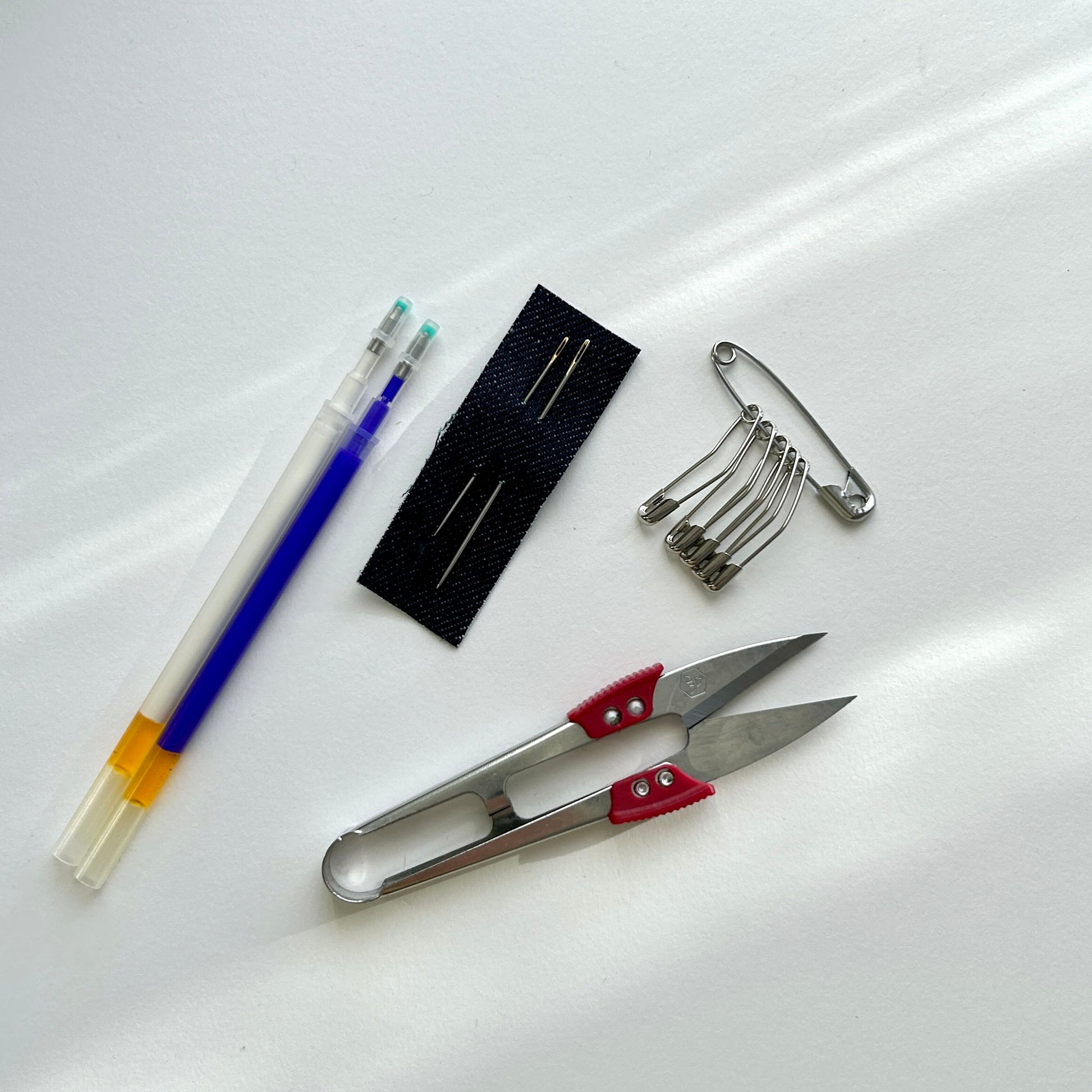 Essential mending tools: heat-erasable pens, sashiko needles, thread snips, and safety pins.