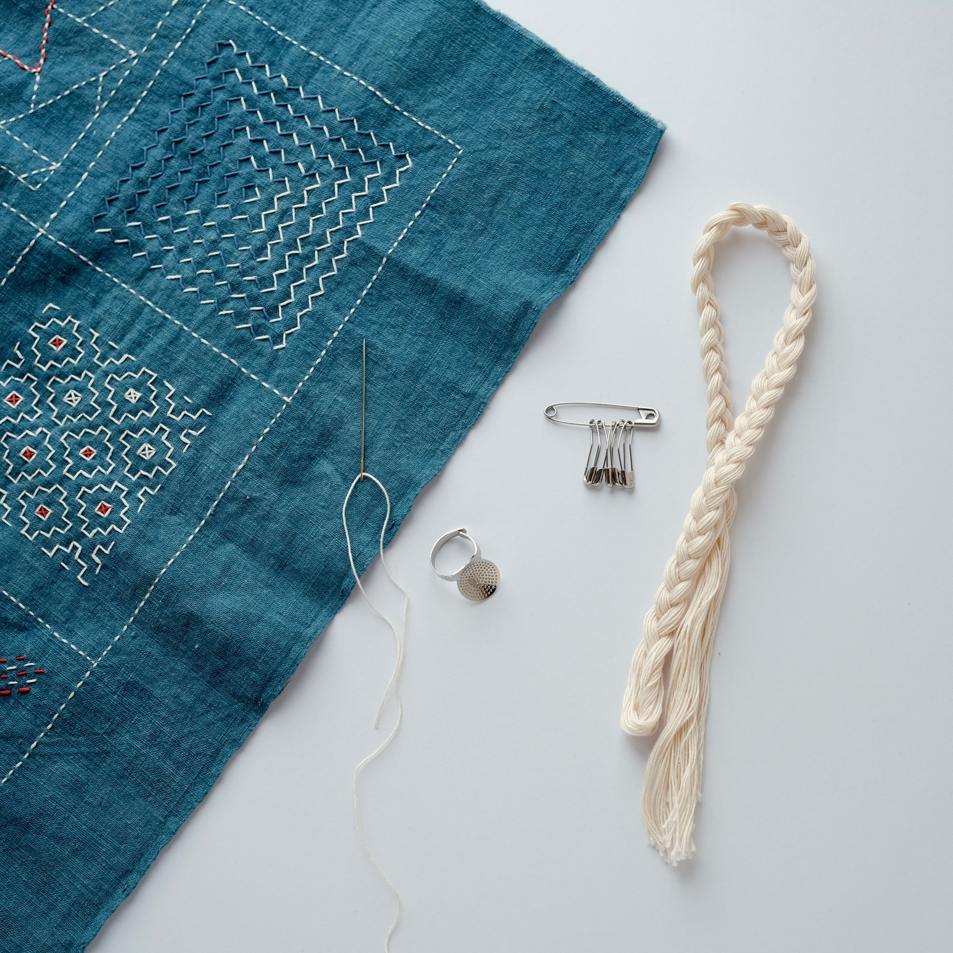 Sashiko needles, safety pins, and off-white thread displayed with a finished Sashiko stitching sample.